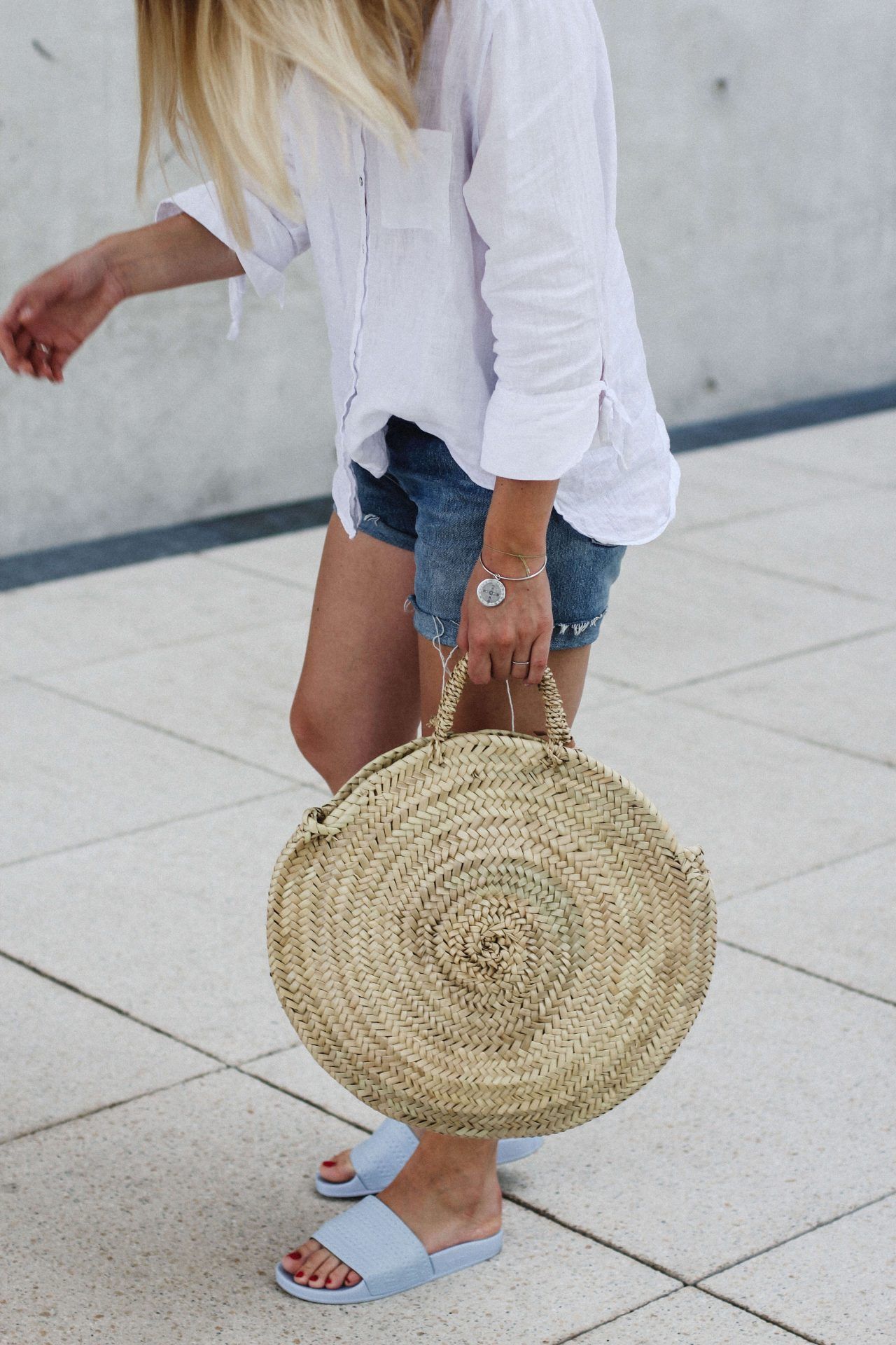 Girl in denim shorts carrying round straw bag