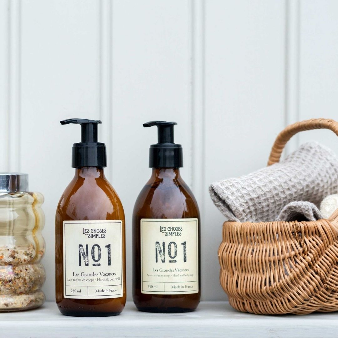 Bottles of Les Grandes Vacances hand soap and hand lotion with basket and towels